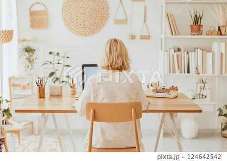 Elderly blonde woman typing on laptop in bright home office with minimalistic design 124642542