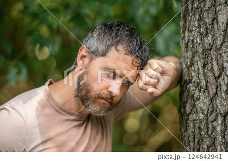 Hispanic mature and brutal bearded man feels tired and sweating after hardworking in the forest leaning on tree outdoor Hispanic mature and brutal bearded man feels tired and sweating after hardworking in the forest leaning on tree outdoor 124642941