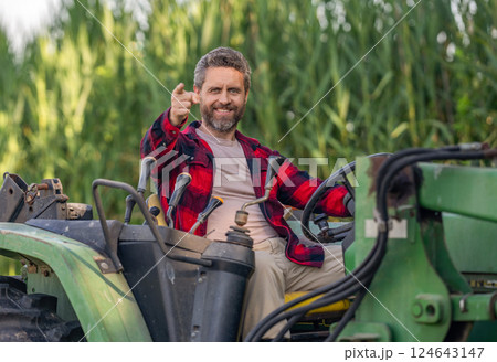 Crop harvesting. Agriculture equipment. Farmer with harvesting machinery. Mature man at tractor. Tractor driver. Agriculture and field work. Farmer in field with tractor outdoor. Point finger 124643147