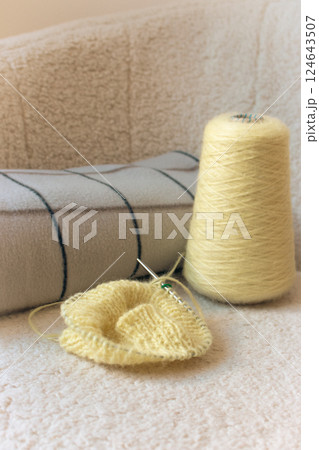 Yellow knitting with grey checkered plaid on sofa. Knitted fashion. Cotton knitting crochet with knitting needles and bobbin. Knitting hobby. Handmade knitted clothing. Cozy still life. Domestic life Yellow knitting with grey checkered plaid on sofa. Knitted fashion. Cotton knitting crochet with knitting needles and bobbin. Knitting hobby. Handmade knitted clothing. Cozy still life. Domestic life 124643507