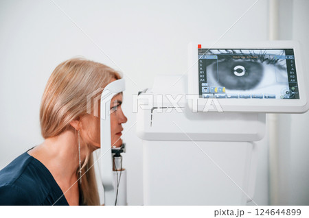 Woman is sitting in the clinic and checking her vision by special device Woman is sitting in the clinic and checking her vision by special device 124644899