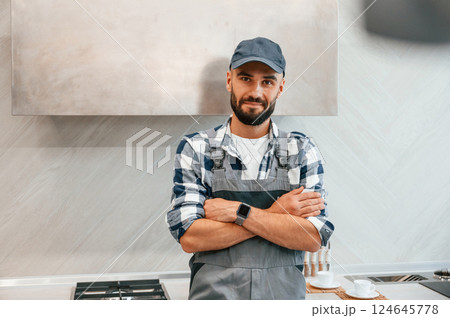 Standing with arms crossed. Plumber in uniform is indoors at home Standing with arms crossed. Plumber in uniform is indoors at home 124645778