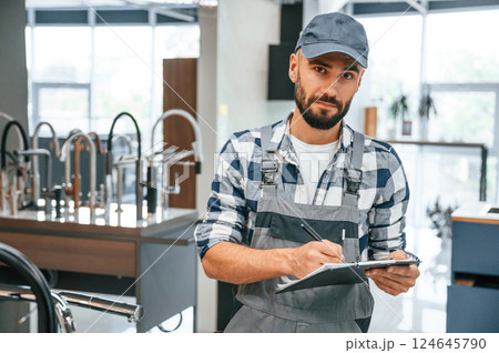 Holding notepad. Plumber in uniform is indoors at home Holding notepad. Plumber in uniform is indoors at home 124645790