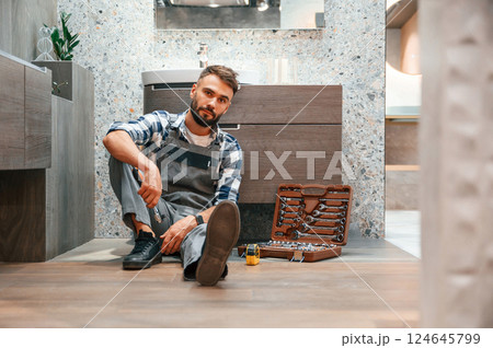On the floor with case of equipment. Plumber in uniform is indoors at home 124645799