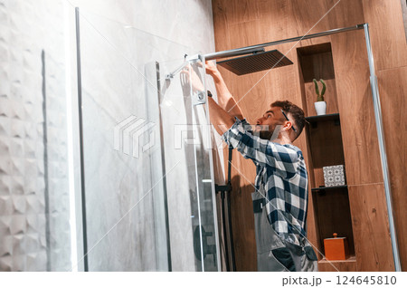 Repairs the shower cabin. Plumber in uniform is indoors at home 124645810
