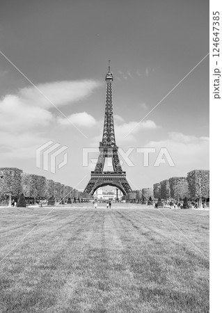 The Eiffel Tower rises majestically over a lush green park, surrounded by meticulously shaped hedges. Visitors stroll leisurely beneath the iconic structure on a sunny day. 124647385
