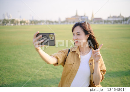 Traveler asian woman in her 30s making a livestream or selfie on smartphone. Immerse yourself in the religious heart of Bangkok with her Thailand adventure. 124648914