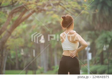 Shoulder pain problem. woman jogger. 30s asian female wearing white sportswear holding her shoulder with pain after running exercise in public park. 124648975