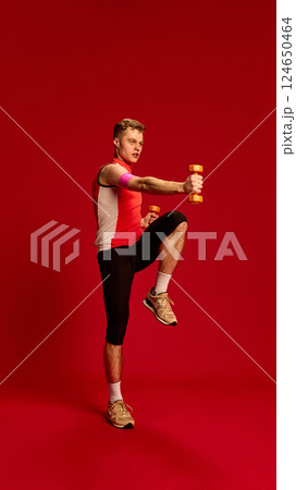 Energetic man doing dynamic punch and knee lift while holding dumbbells, showing coordination and explosive movement in active pose. Energetic man doing dynamic punch and knee lift while holding dumbbells, showing coordination and explosive movement in active pose. 124650464
