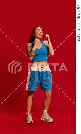 Dynamic photo of young female athlete parrying punches during martial arts training. Girl stands in basic position against red studio background. 124650497