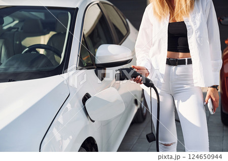 Waiting automobile to charge. Young woman in white clothes is with her electric car at daytime 124650944