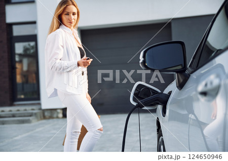 Waiting automobile to charge. Young woman in white clothes is with her electric car at daytime 124650946