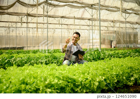 Smiling farmer using digital tablet while inspecting crops in a greenhouse. Concept of modern agriculture Smiling farmer using digital tablet while inspecting crops in a greenhouse. Concept of modern agriculture 124651090