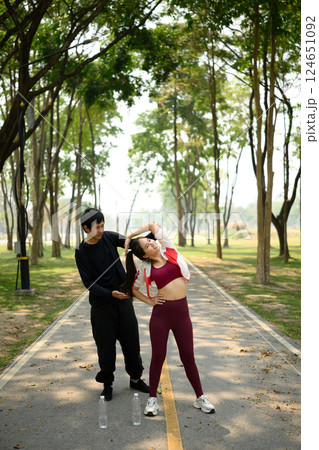 Athletic couple stretching together before a run on a sunlit park path 124651092