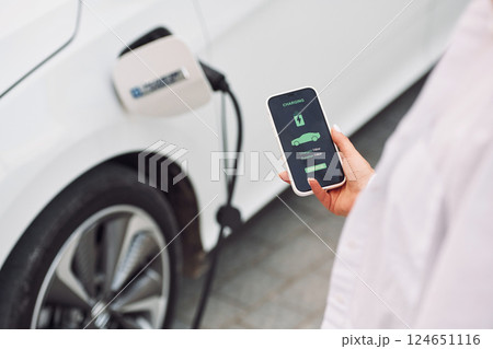 Close up view. Woman charging her electric car and monitoring process on smartphone 124651116