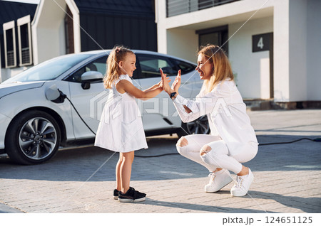 Having fun, playing together. Young woman with her little daughter is with their electric car outdoors 124651125