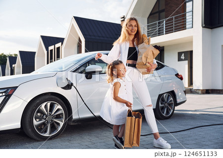 Charging the vehicle together. Young woman with her little daughter is with their electric car outdoors 124651133