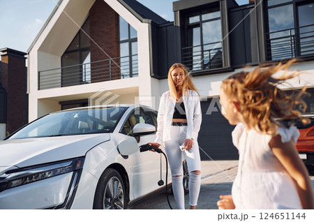 Young woman with her little daughter is with their electric car outdoors Young woman with her little daughter is with their electric car outdoors 124651144