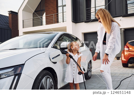 Young woman with her little daughter is with their electric car outdoors 124651148