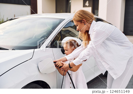 Young woman with her little daughter is with their electric car outdoors 124651149