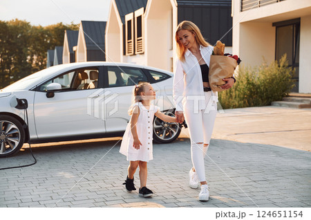 Just from a shopping. With bag. Young woman with her little daughter is with their electric car outdoors 124651154