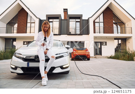 Near the home. Young woman in white clothes is with her electric car at daytime 124651175