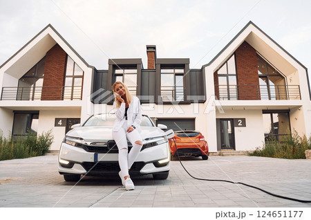 Near the home. Young woman in white clothes is with her electric car at daytime 124651177