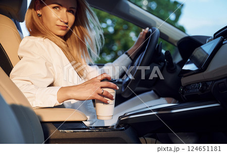 With cup of drink. Young woman in white clothes is with her electric car at daytime 124651181