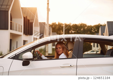 Sitting and looking at the camera. Young woman in white clothes is with her electric car at daytime 124651184