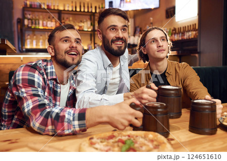Front view. Soccer fans. Three friends are in the bar drinking beer and having a good time Front view. Soccer fans. Three friends are in the bar drinking beer and having a good time 124651610