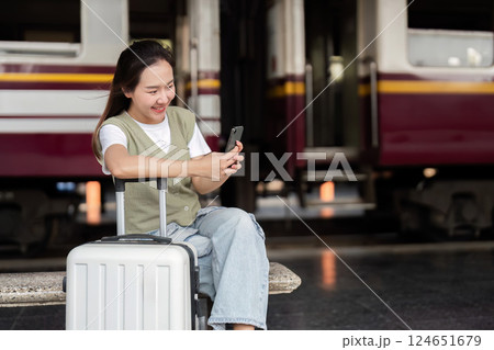 Travel and Communication. A young traveler engaging with her smartphone while waiting at a train station. 124651679