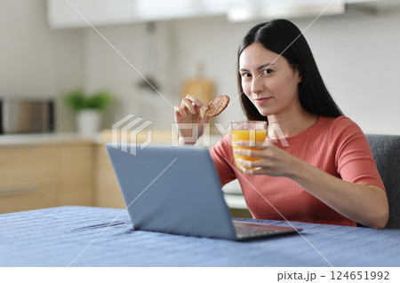 Asian woman holding cookie and orange juice with a laptop Asian woman holding cookie and orange juice with a laptop 124651992