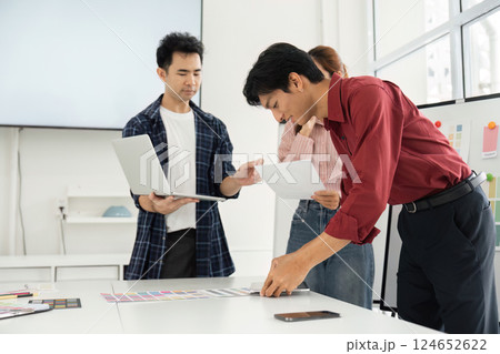 Creative Teamwork and Color Coordination. A team collaborates on color choices while one member assesses design options on a laptop. 124652622