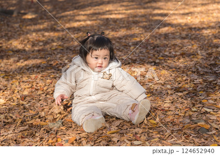 【落ち葉で敷き詰められた冬の公園で遊ぶ1歳児　座る】 124652940