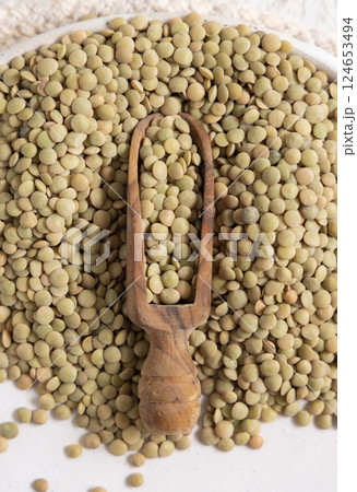 Plate full of dried raw green lentils with a wooden scoop on white table top view. Vegetarian food Plate full of dried raw green lentils with a wooden scoop on white table top view. Vegetarian food 124653494