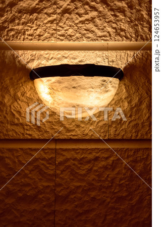 Warm-lit semi-spherical sconce on natural stone surface 124653957