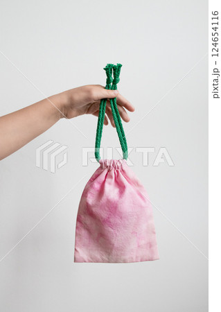 Hand holding pink fabric pouch with green cotton drawstring against white background Hand holding pink fabric pouch with green cotton drawstring against white background 124654116
