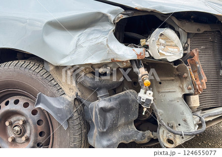 A close-up of a damaged car shows a crumpled fender, exposed headlight components, and bent metal after a collision A close-up of a damaged car shows a crumpled fender, exposed headlight components, and bent metal after a collision 124655077