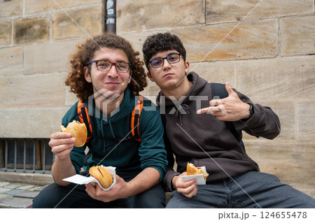 Nuremberg,Germany,August 1, 2023. Two young Caucasians enjoy a break eating sandwiches with the typical Nuremberg sausage. They look at the camera smiling and making faces. Relaxation, friendship. 124655478