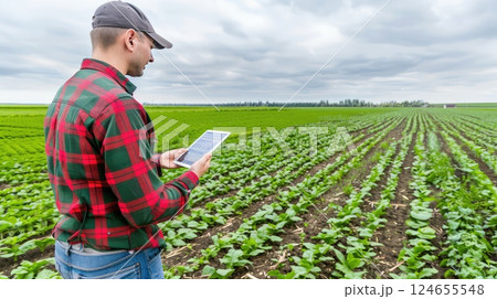 A farmer with a smartphone or tablet PC in a field. He records the results of sowing. A farmer stands in the field with a smartphone, documenting the flourishing crops after sowing. 124655548