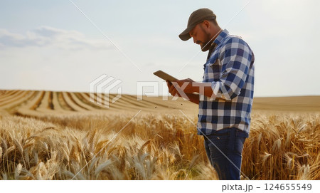 A farmer with a smartphone or tablet PC in a field. He records the results of sowing. A farmer uses his smartphone to record the successful results of sowing in the vibrant field. 124655549