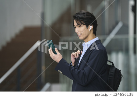 スマホの画面を見るイヤホンをした若いビジネスマン 124656139