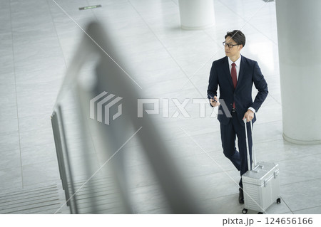 スマートフォンとキャリーケースを持って歩く40代のビジネスマン スマートフォンとキャリーケースを持って歩く40代のビジネスマン 124656166