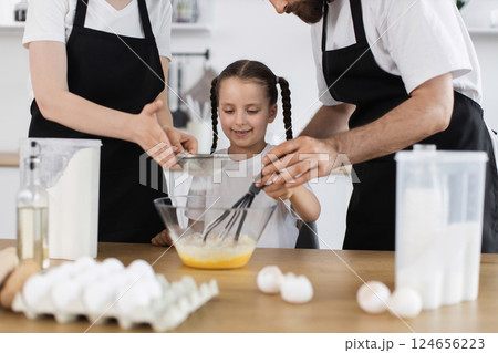 Caucasian family with parents and daughter cooking together in modern kitchen, smiling and enjoying activity Caucasian family with parents and daughter cooking together in modern kitchen, smiling and enjoying activity 124656223