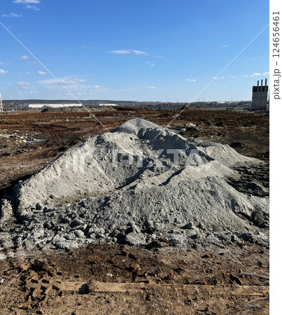 Large pile of gravel at a construction site under a clear blue sky. Industrial area in the background with construction materials scattered on the ground, active work zone Large pile of gravel at a construction site under a clear blue sky. Industrial area in the background with construction materials scattered on the ground, active work zone 124656461