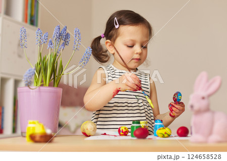 Little child girl paint Easter eggs at home. kid is preparing for Easter. 124658528