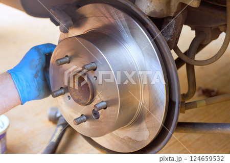 Worker is replacing brake rotor in an auto service, demonstrating hands on mechanical skills at vehicle maintenance. 124659532