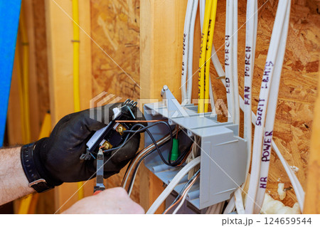 An electrician is connecting wires to switch light in junction box while preparing for electrical service installation An electrician is connecting wires to switch light in junction box while preparing for electrical service installation 124659544