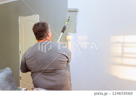 Paint worker painting wall gray over white in bright room, showing renovation in progress. 124659560