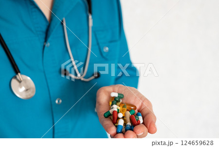 Health professional holds various pills and capsules while wearing a stethoscope 124659628